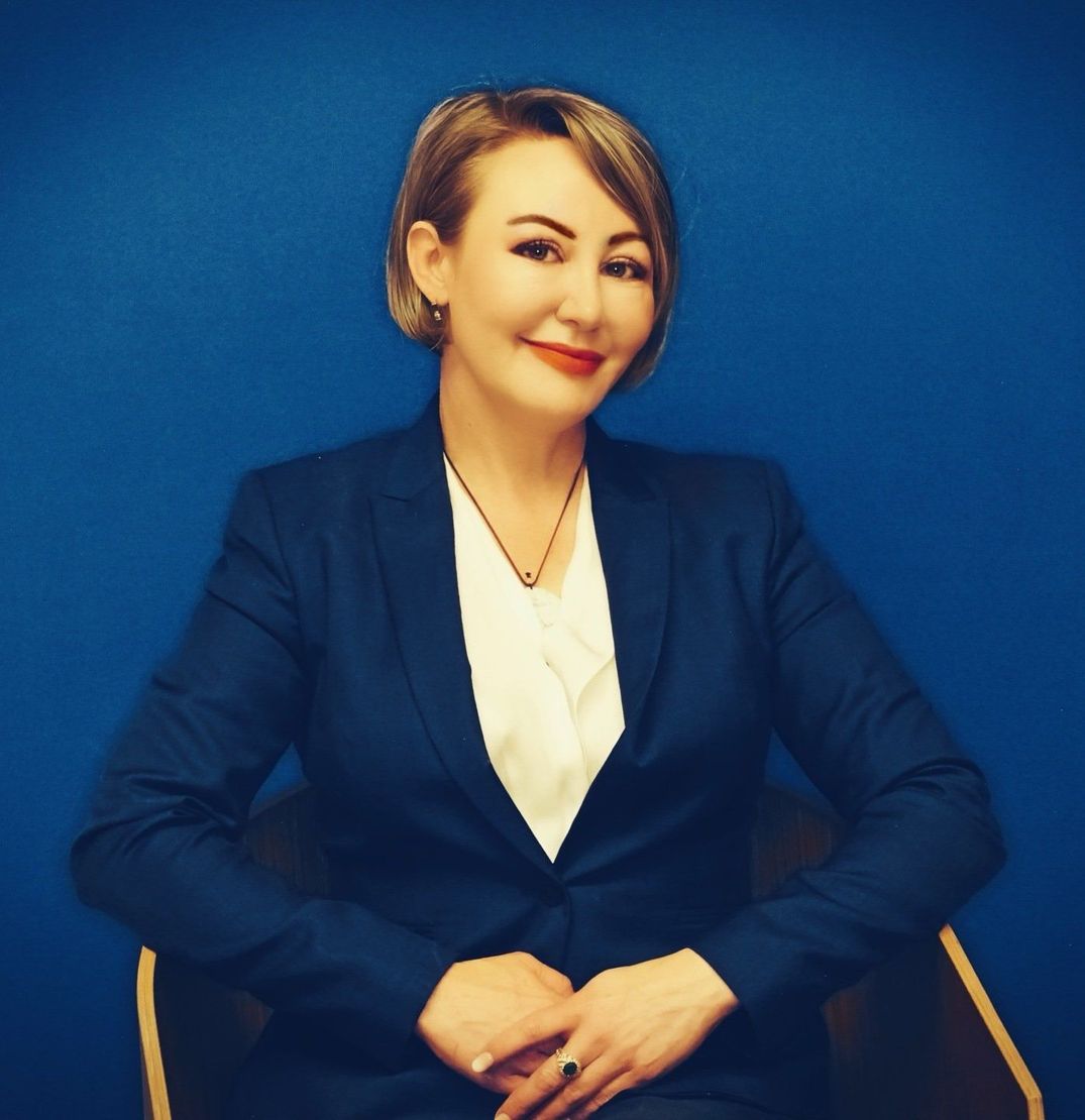 A woman in a blue suit is sitting in front of a blue wall