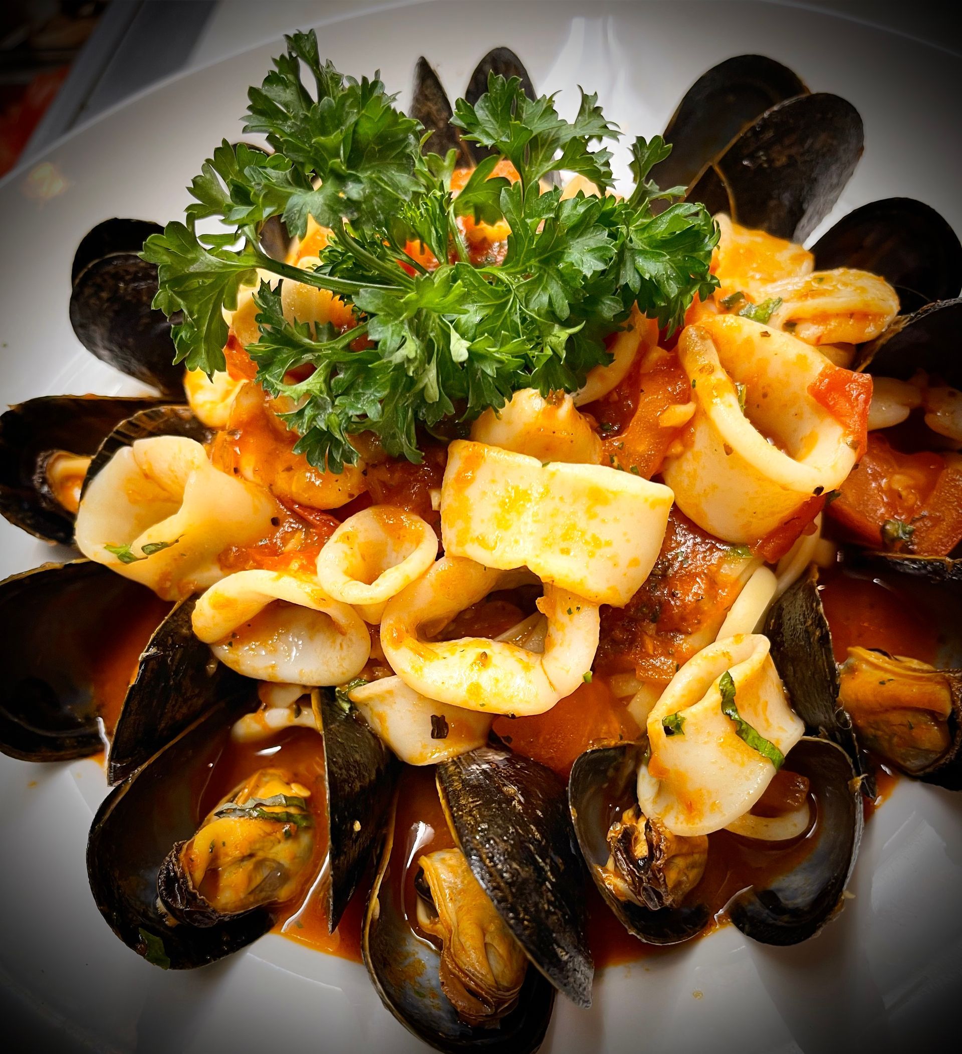 A plate of seafood with sauce and parsley on top