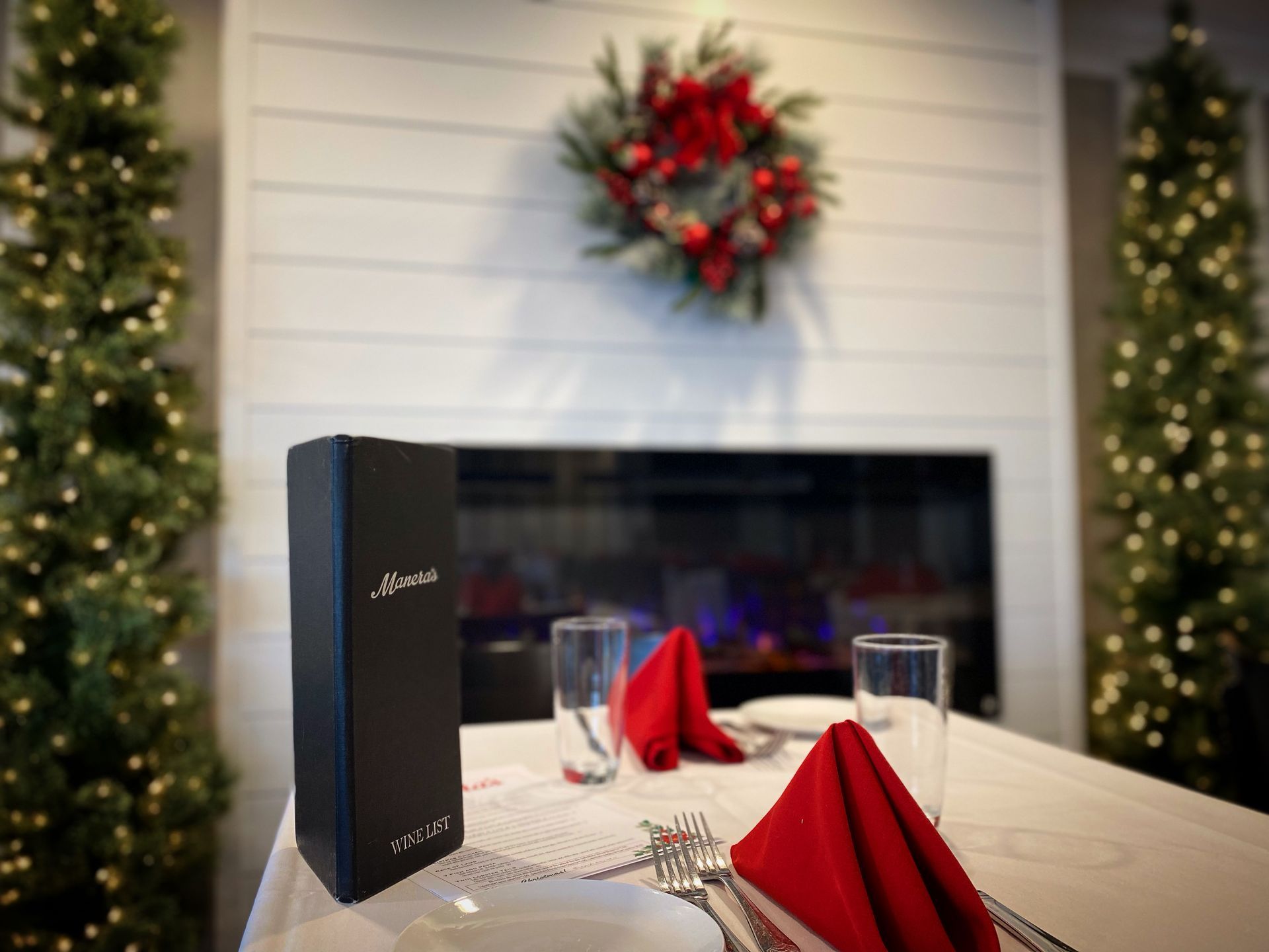 A table set for a christmas dinner with a wreath on the wall behind it.