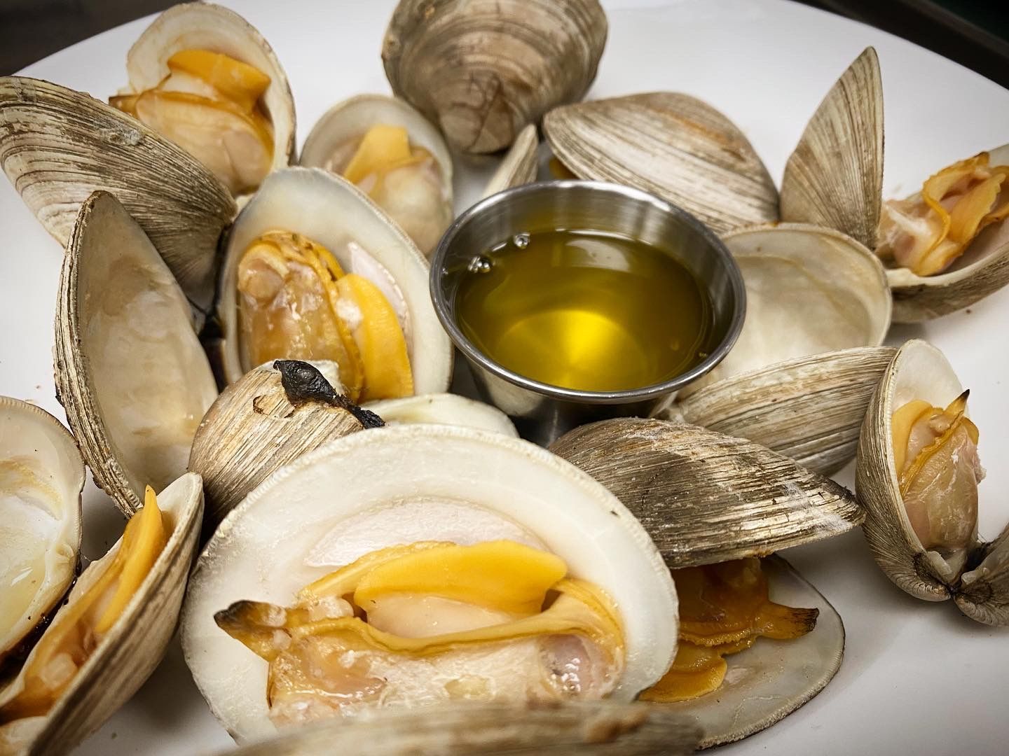 A white plate topped with clams and a small cup of oil