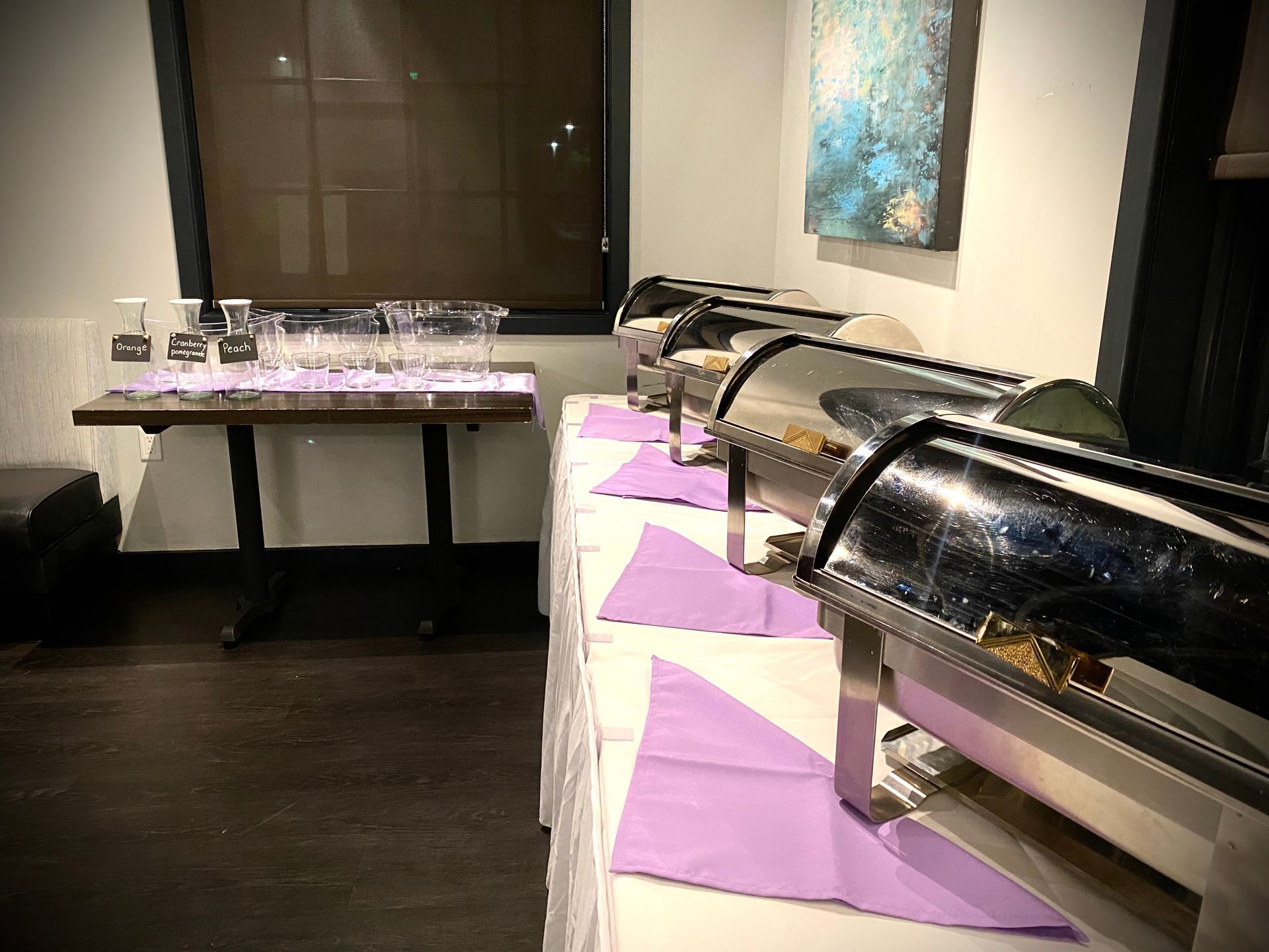 A room with a buffet table and a window with a painting on the wall.