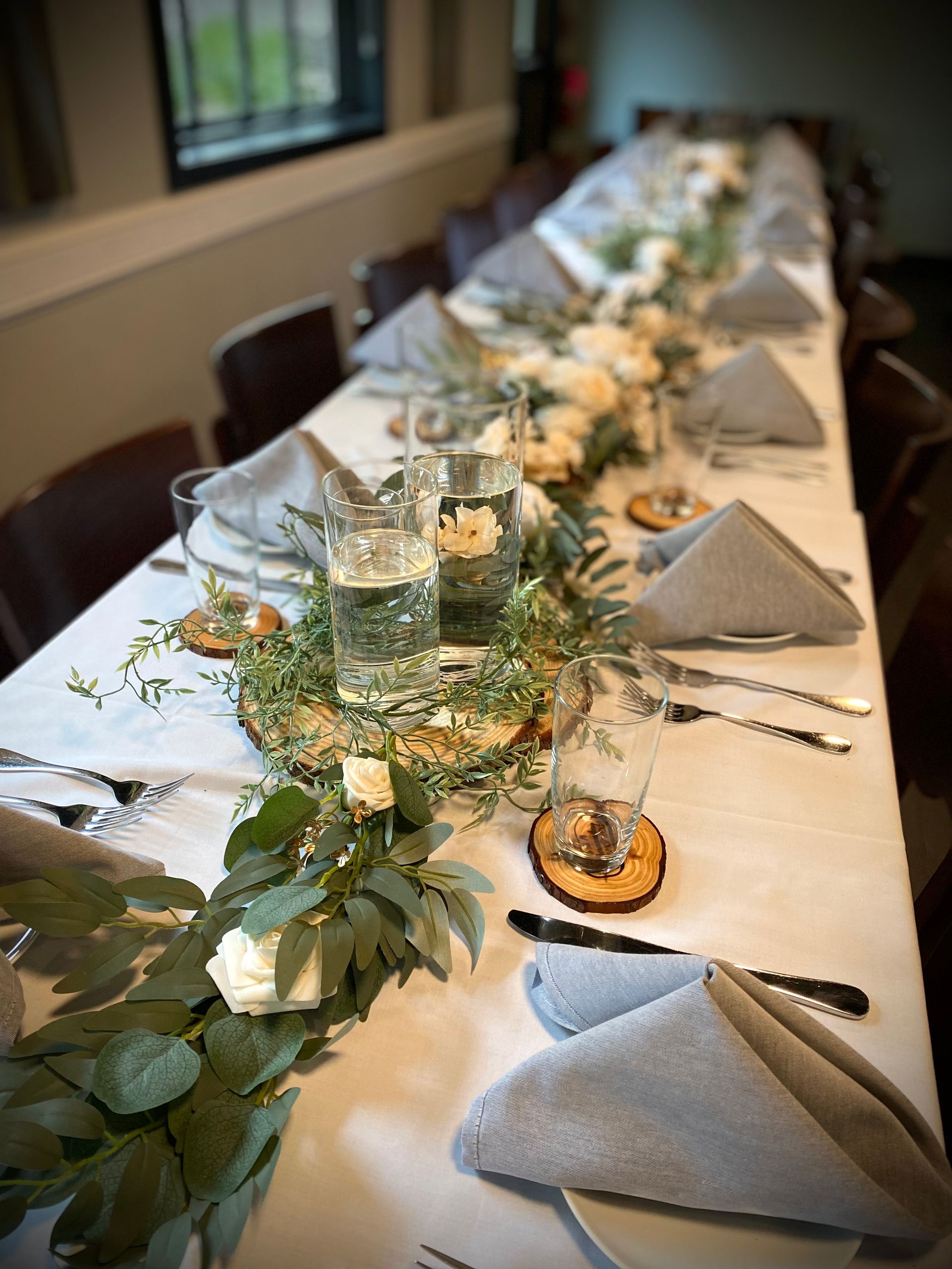 A long table with plates , napkins , utensils and flowers on it.