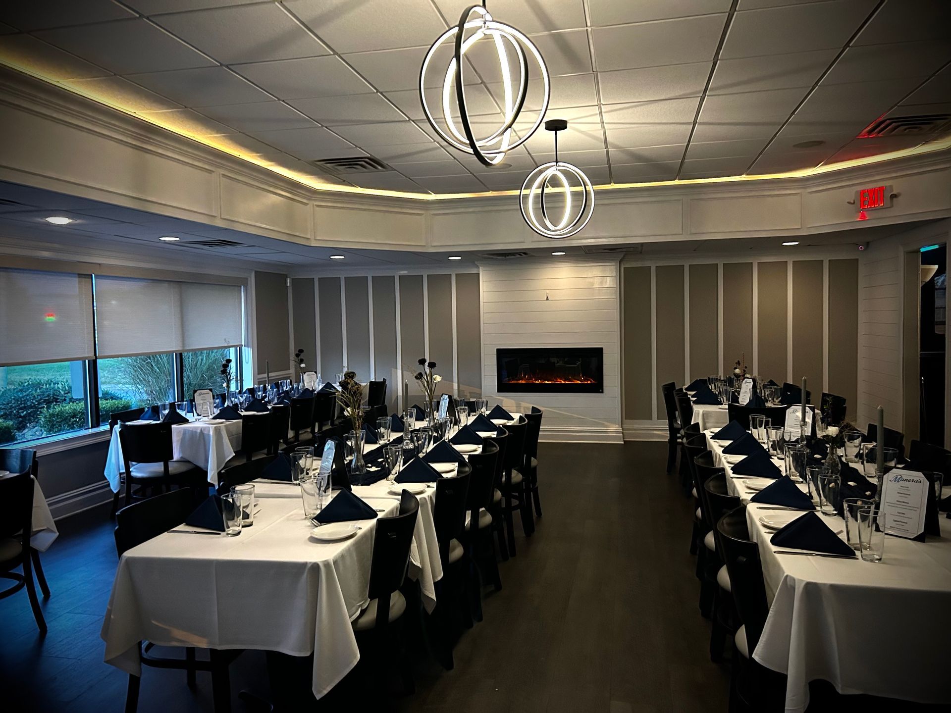 A long dining room with tables and chairs and a fireplace.