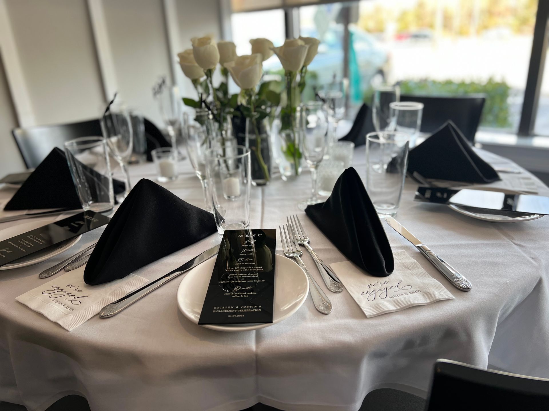 A table set for a wedding reception with black napkins , silverware , plates , and a menu.