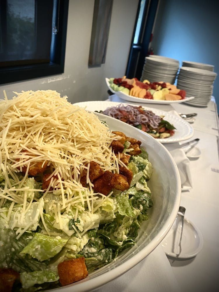 A caesar salad is sitting on a table next to a plate of fruit.