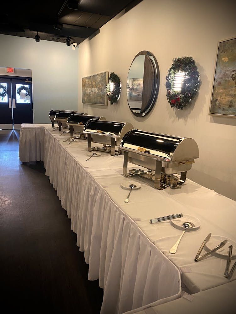 A long buffet line in a room with white tables and utensils.