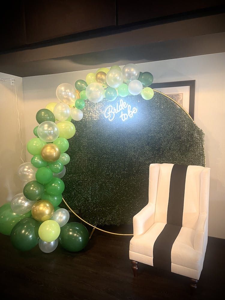 A room decorated with green and gold balloons and a chair.