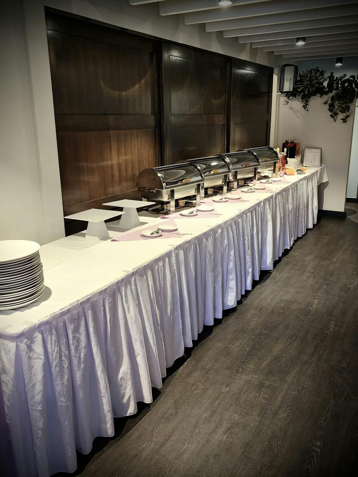 A long buffet table with white curtains and plates on it.