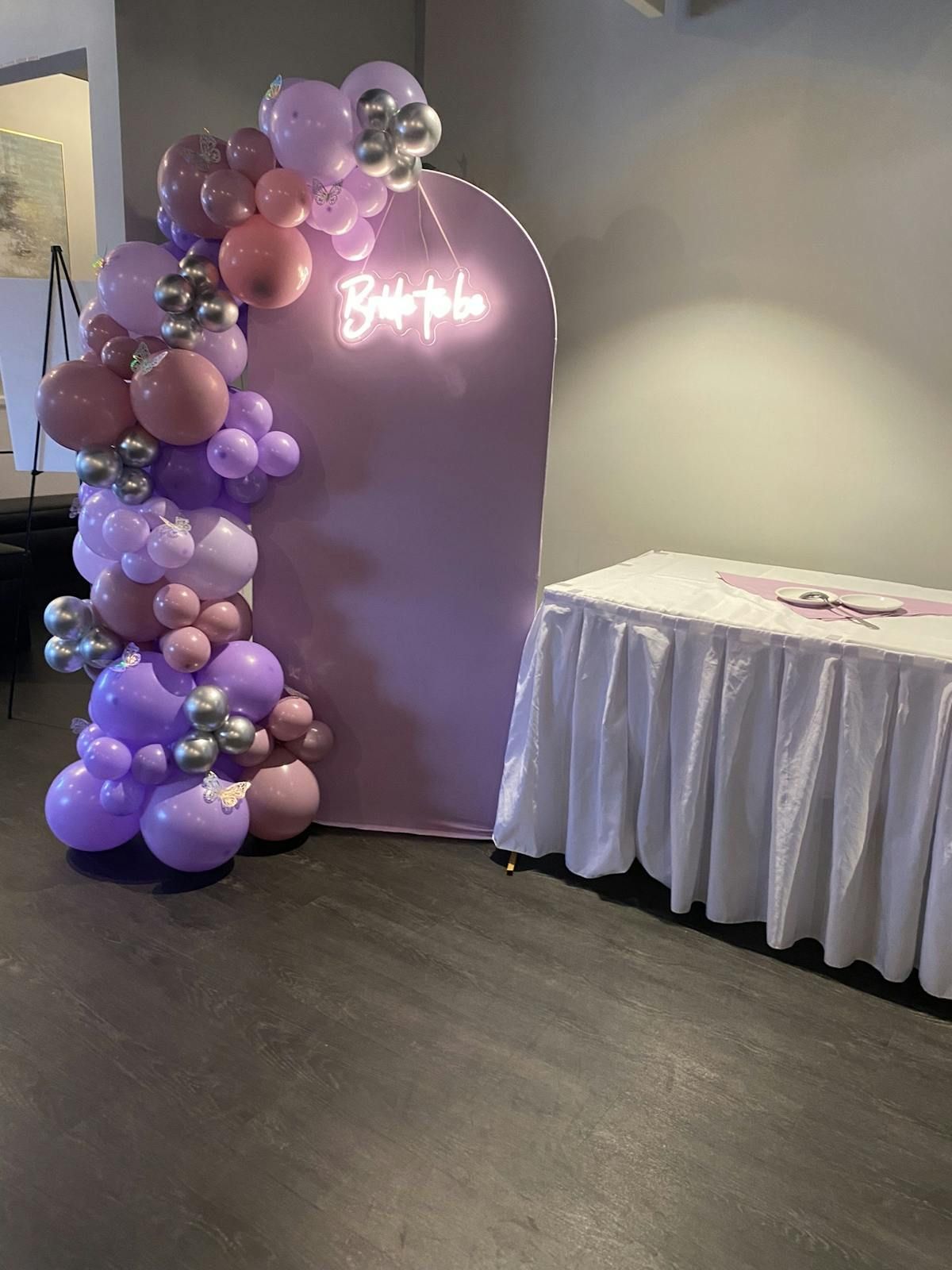 A room with balloons , a table and a neon sign.