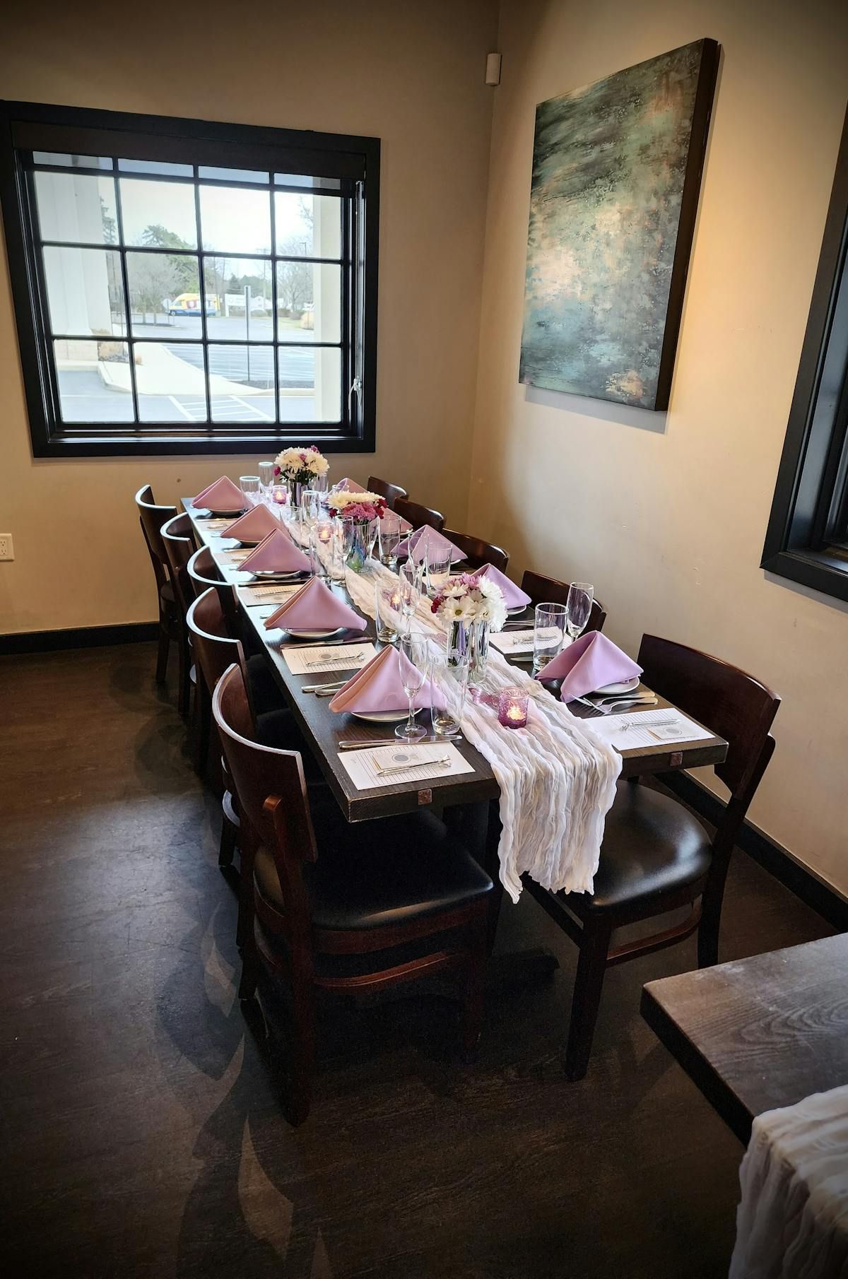 A long table with plates , napkins and glasses in a room with a window.