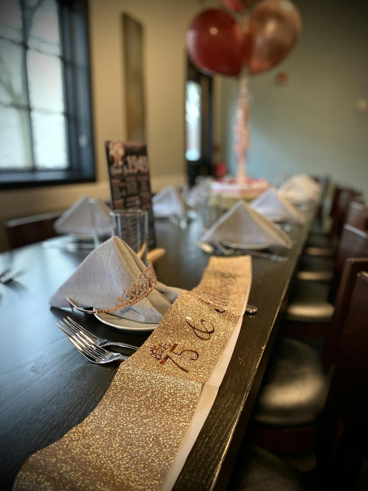 A long table with plates , silverware , and balloons on it.