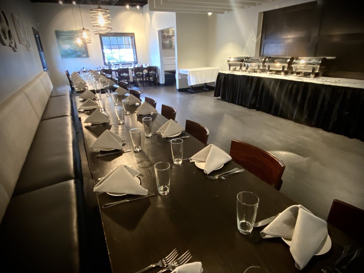 A long table in a restaurant with glasses and napkins on it.