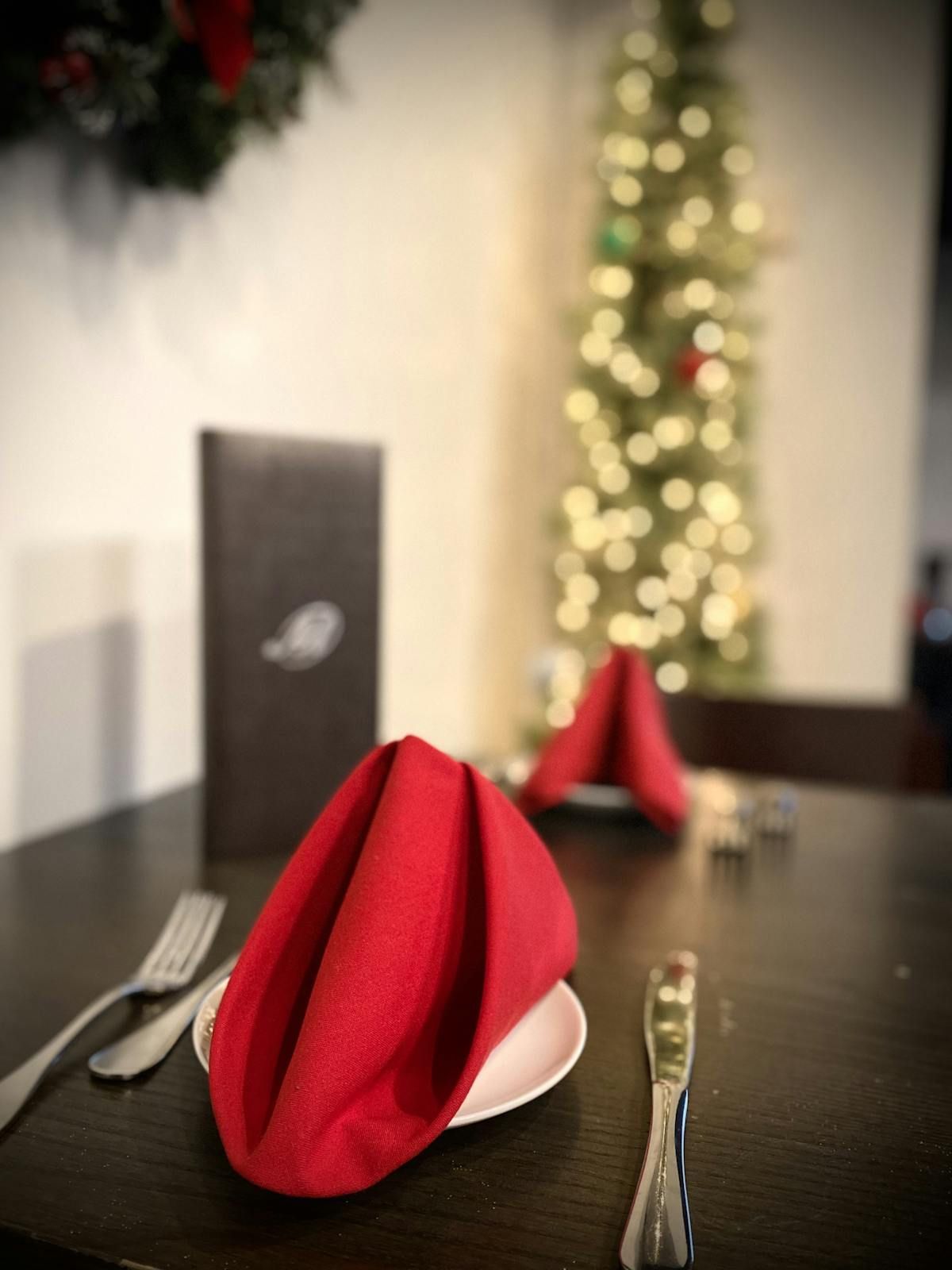 A table with red napkins and silverware and a christmas tree in the background