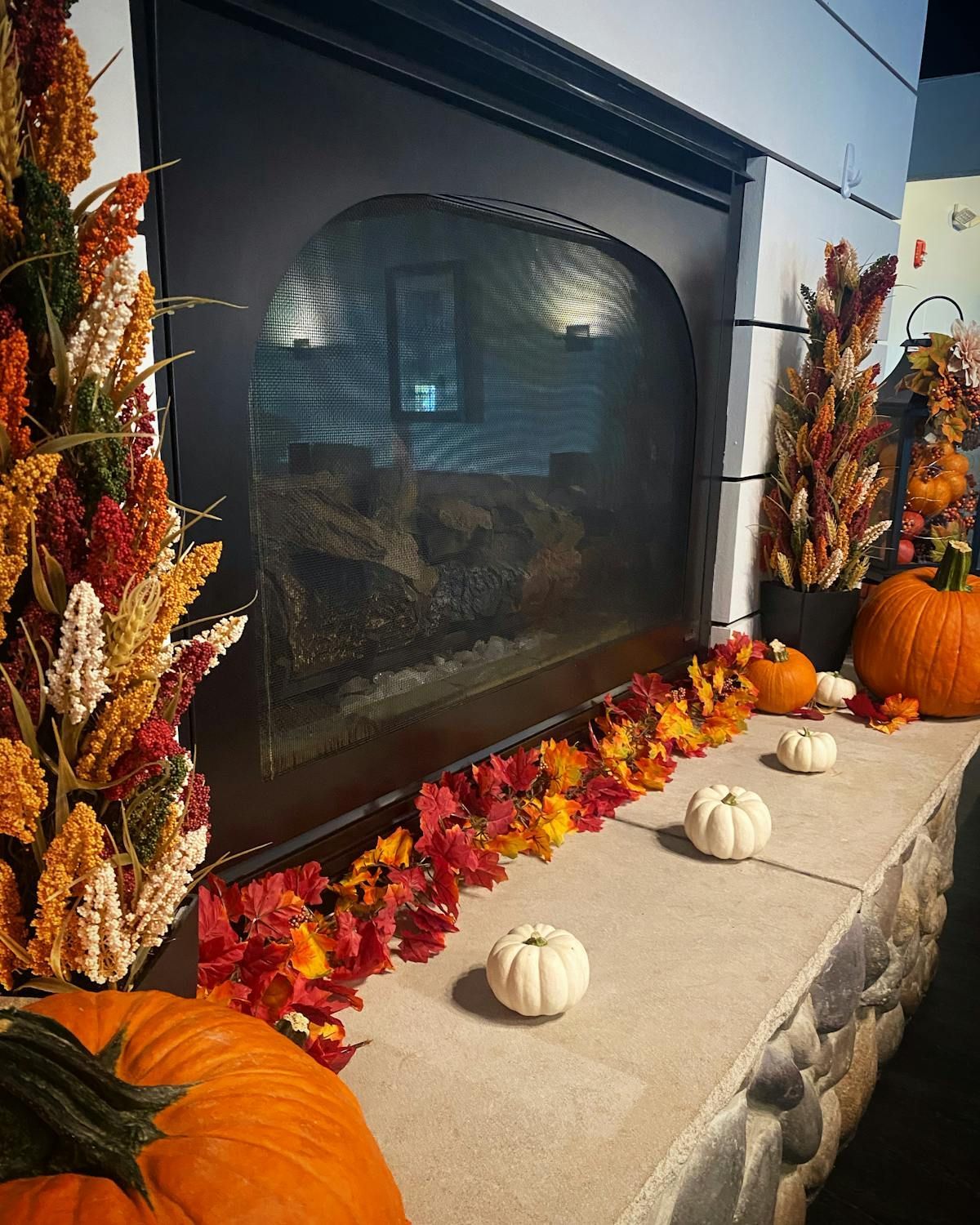 A fireplace decorated for fall with pumpkins and leaves