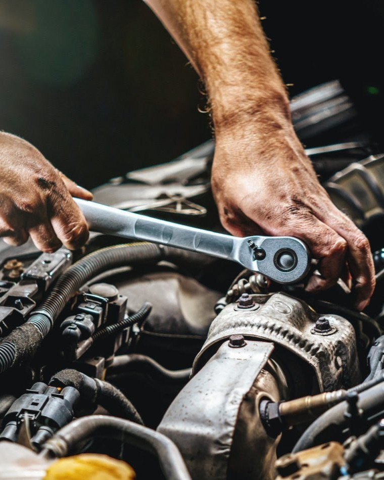 A man is working on a car engine with a wrench | B&B Automotive Services