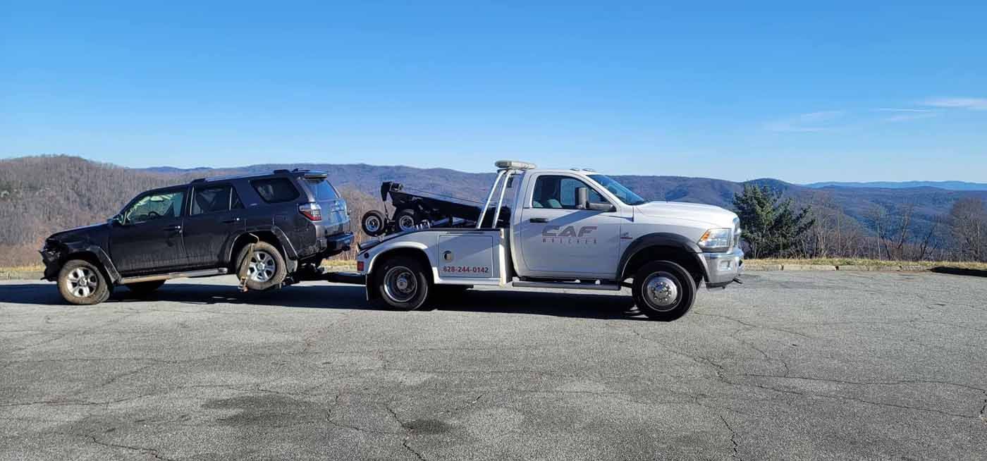 A tow truck is towing a black suv in a parking lot.