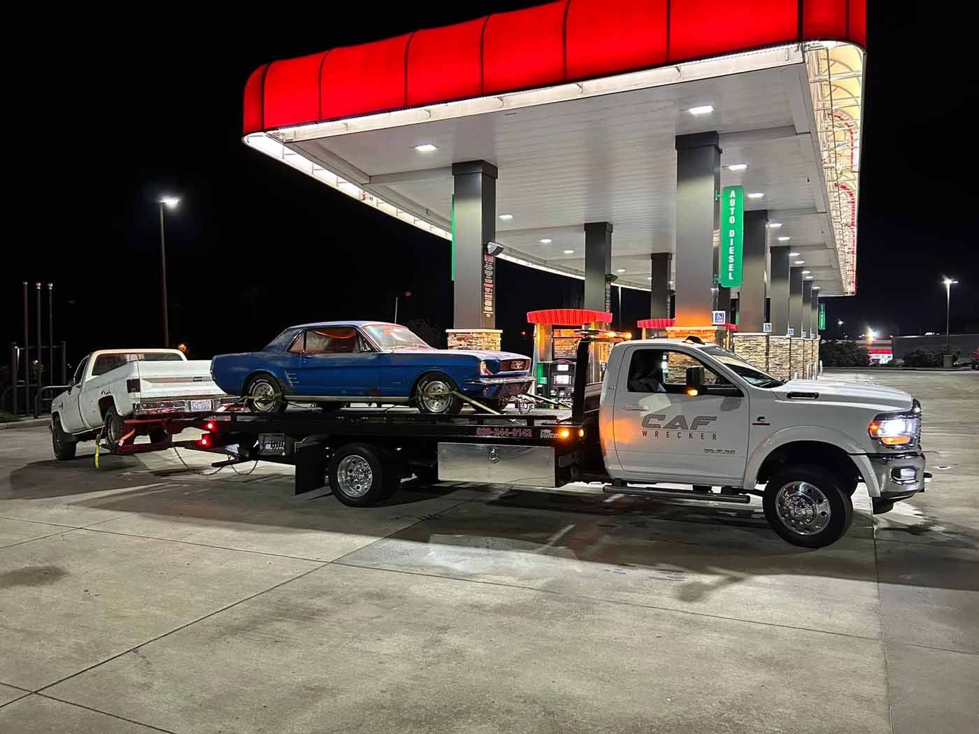 A tow truck is carrying a blue car to a gas station.