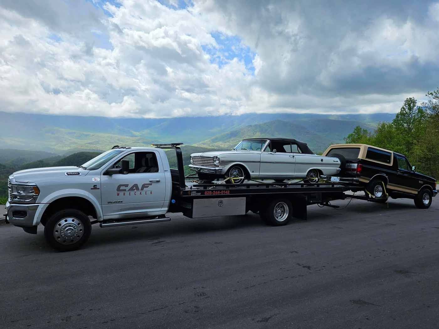 A tow truck is carrying two cars on a trailer.