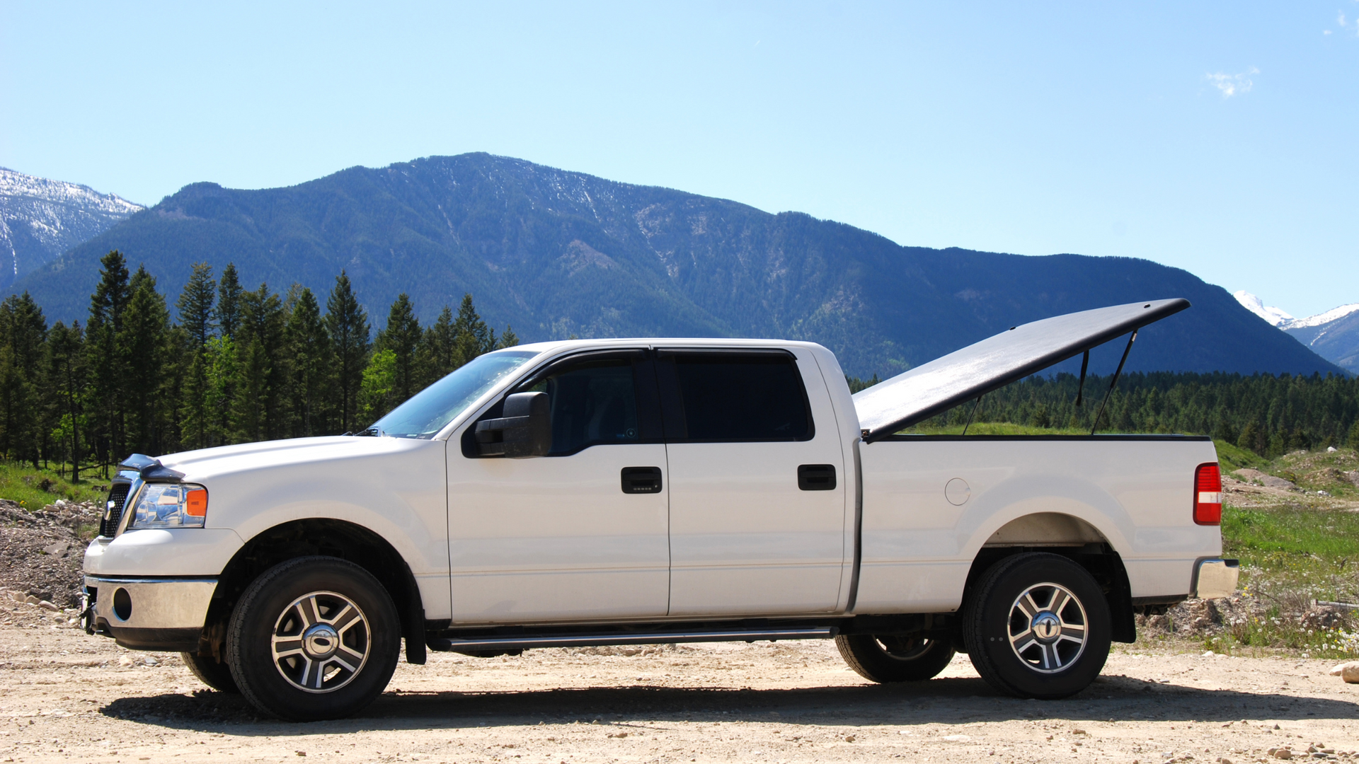 A white truck is parked on a dirt road with mountains in the background