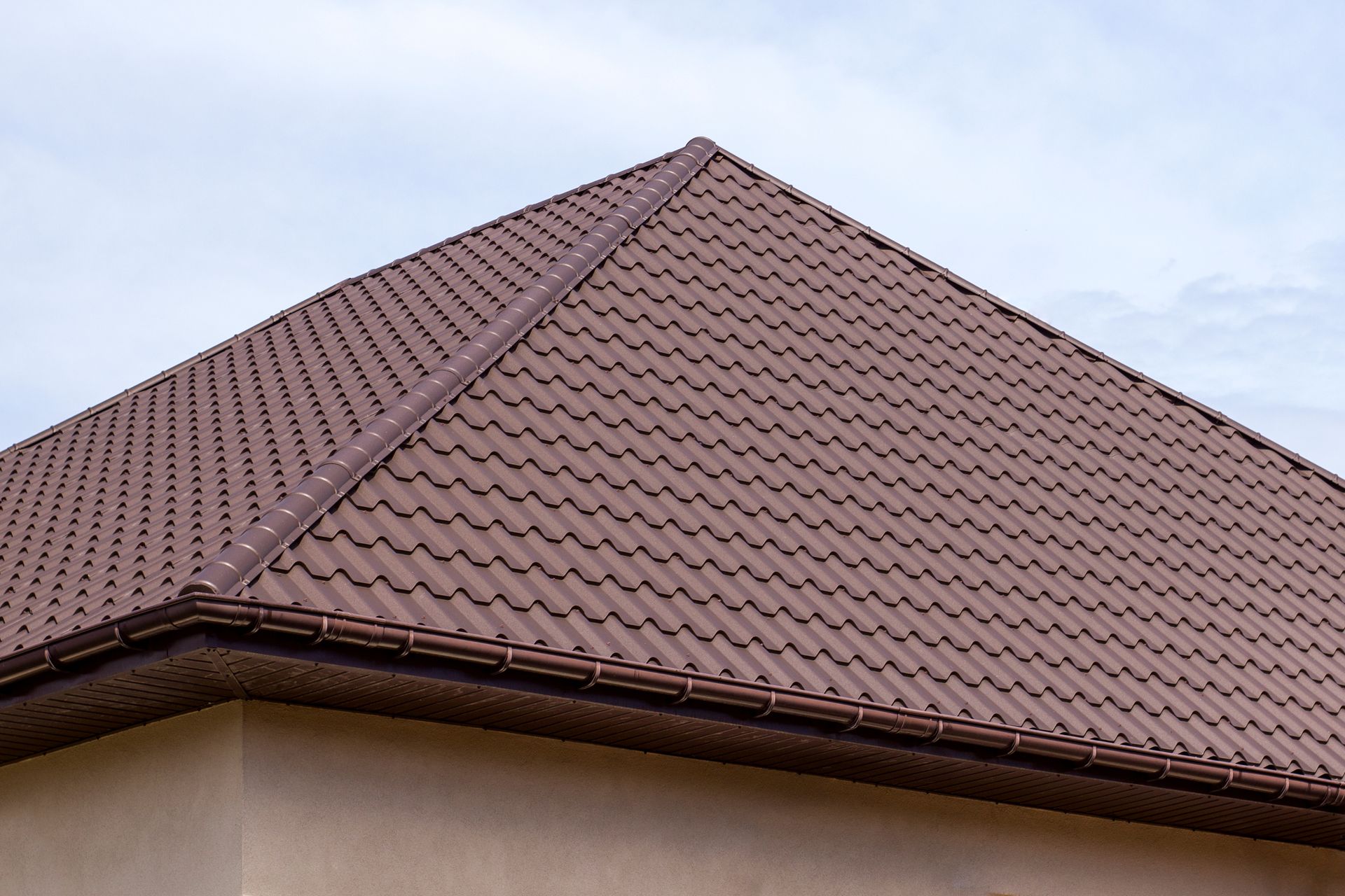 A brown, textured hip roof on a building against a pale sky.
