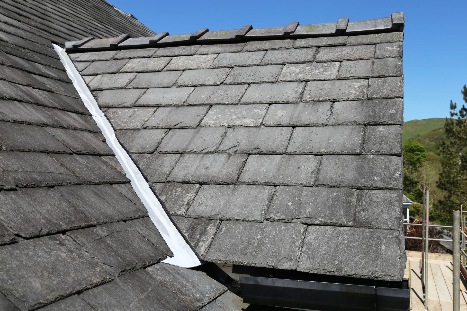 A gray tiled roof section with a silver metal flashing strip angled along the joint where the two roof planes meet.