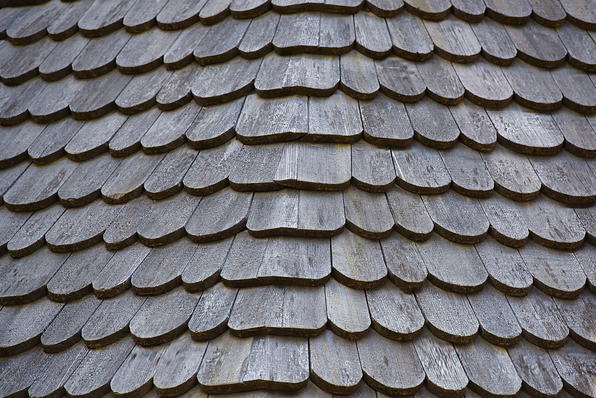A close-up view of a roof covered in weathered, grey wooden shingles arranged in overlapping rows.