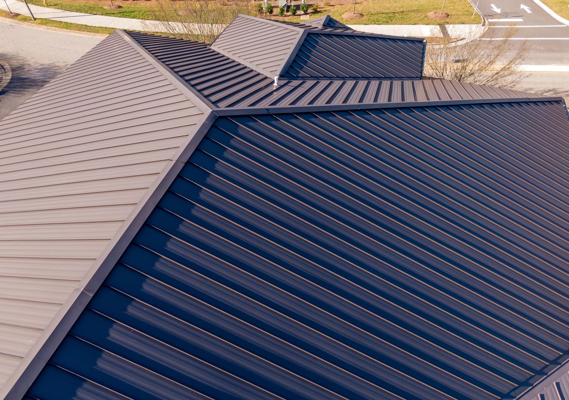 An aerial, high-angle view of a modern dark blue metal roof with multiple sloped sections and ridgelines.