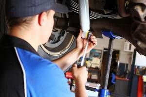 A mechanic uses a wrench to tighten a bolt on a vehicle's suspension system in an automotive repair shop.
