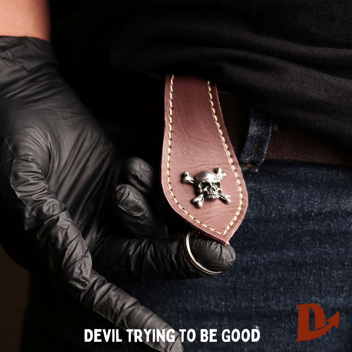 A silver-toned oval belt buckle featuring a skull and motorcycle imagery, resting on a small wooden crate.