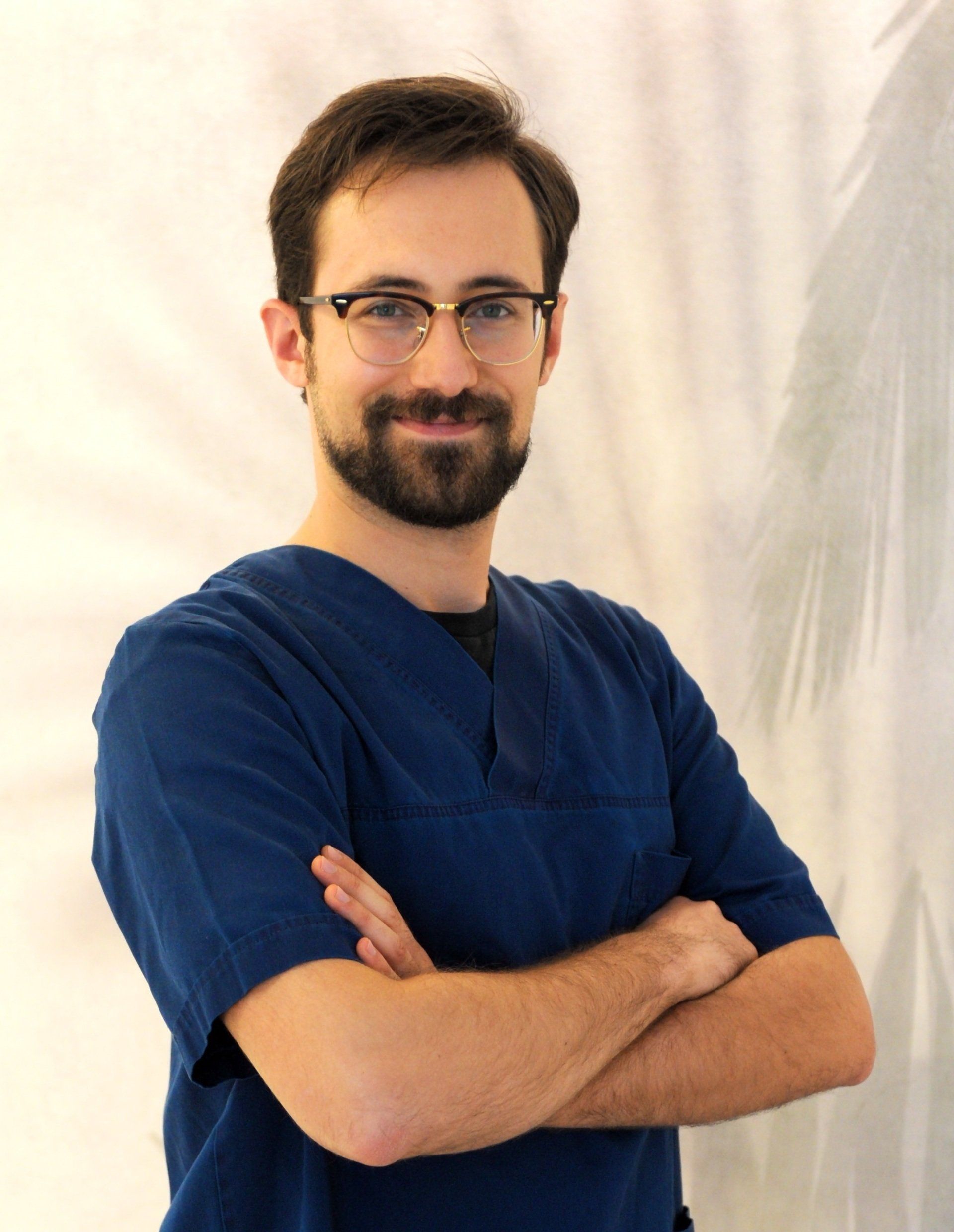 Un uomo che indossa occhiali e un camice blu è in piedi con le braccia incrociate