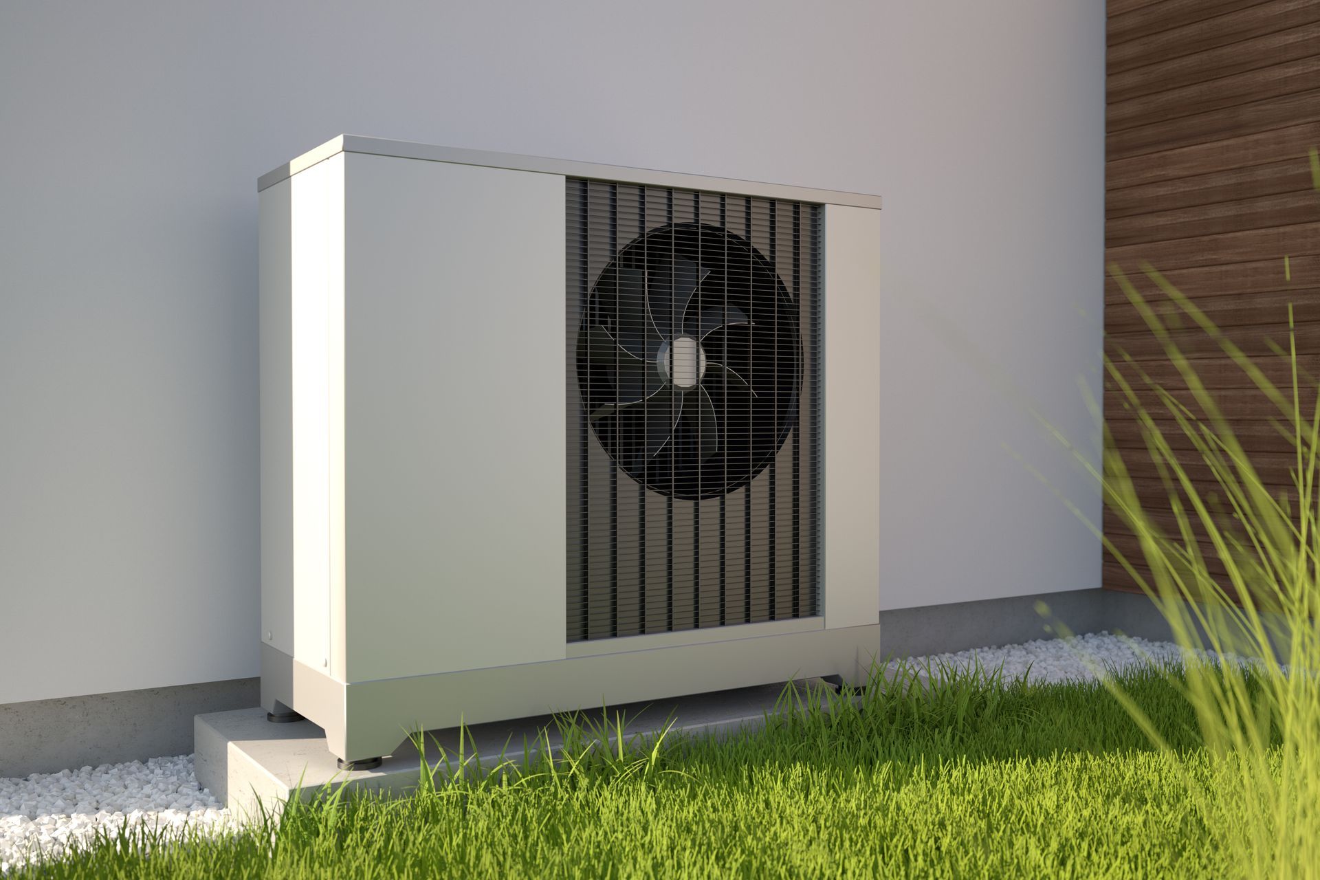 A white outdoor heat pump unit sits on a concrete base against a white wall in a garden setting.