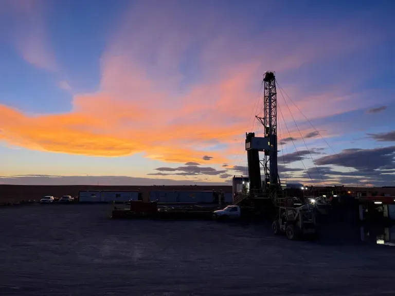 There is a sunset in the background and a drilling rig in the foreground.