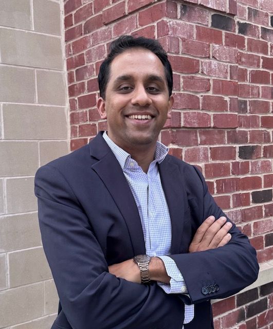 A woman is sitting at a desk with a laptop and a vase of flowers.
