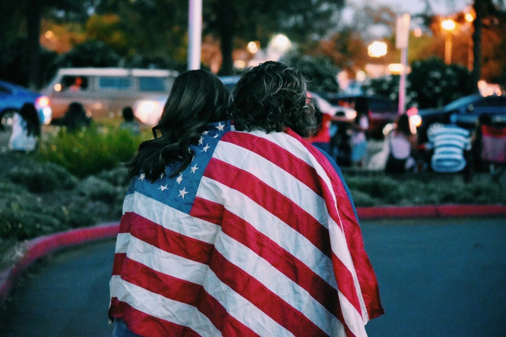 A man and a woman are standing next to each other wrapped in an american flag.