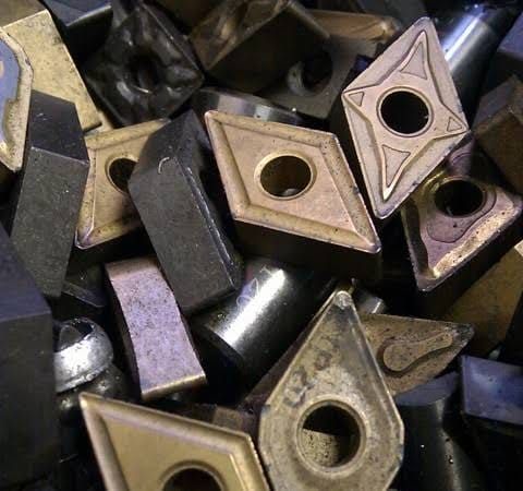 Montón de plaquitas de corte para torno de metal en tonos negro y dorado con orificios centrales circulares