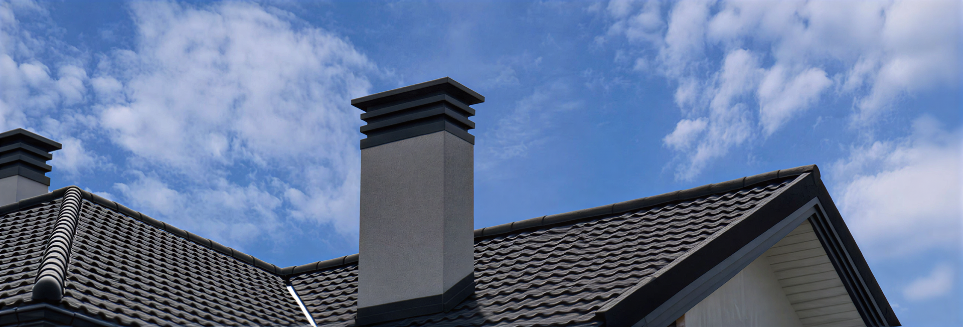 Chimney on a house roof against a partly cloudy blue sky.