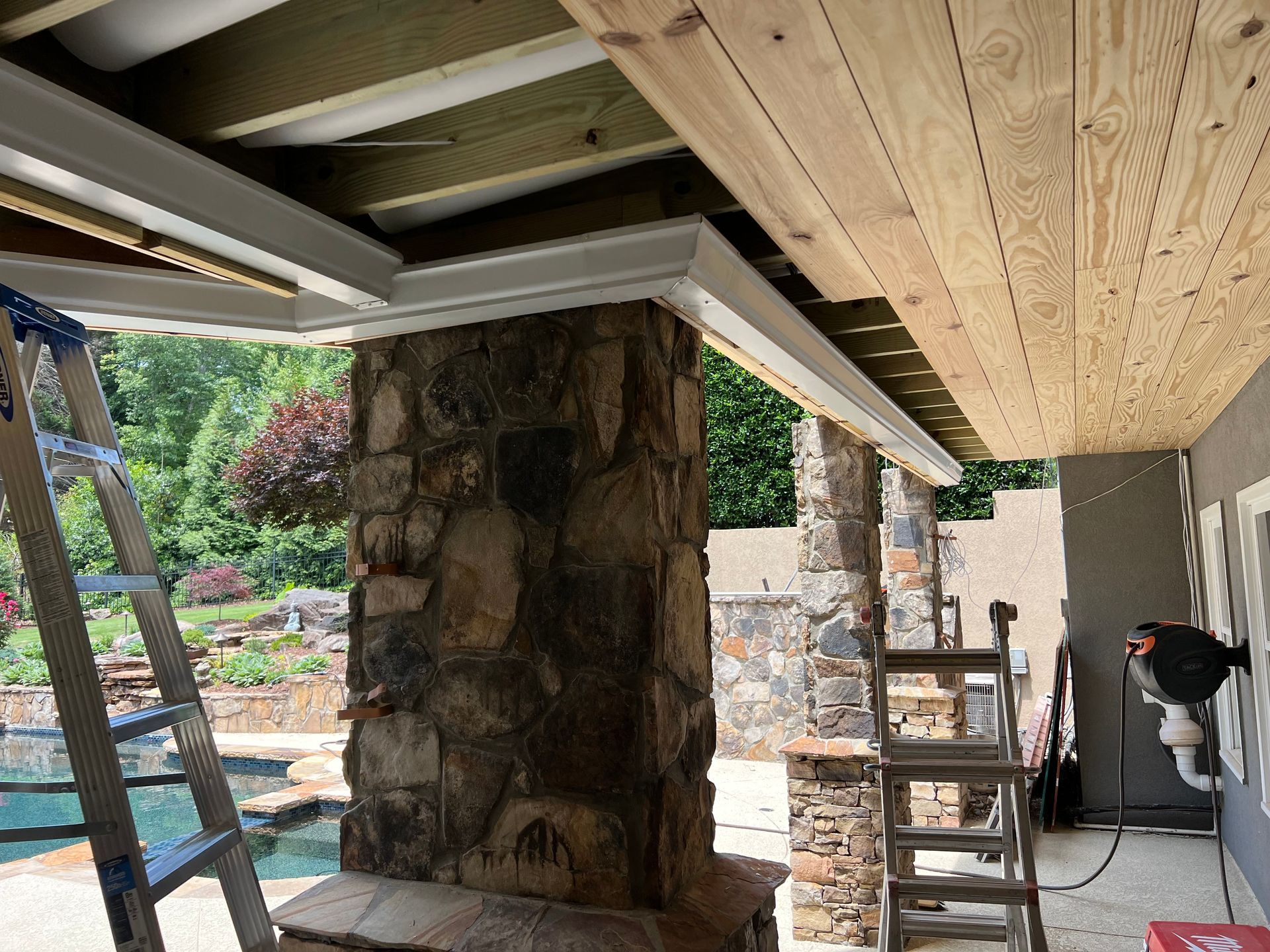 A ladder is sitting under a wooden ceiling next to a stone wall.