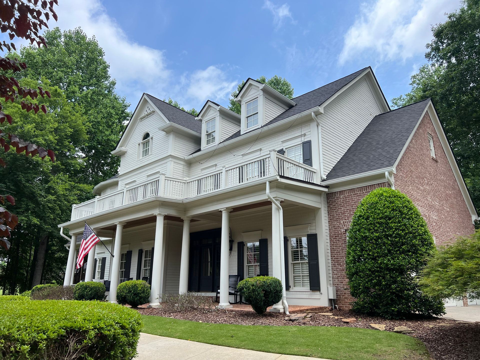 A large white house with a black roof is surrounded by trees and bushes.