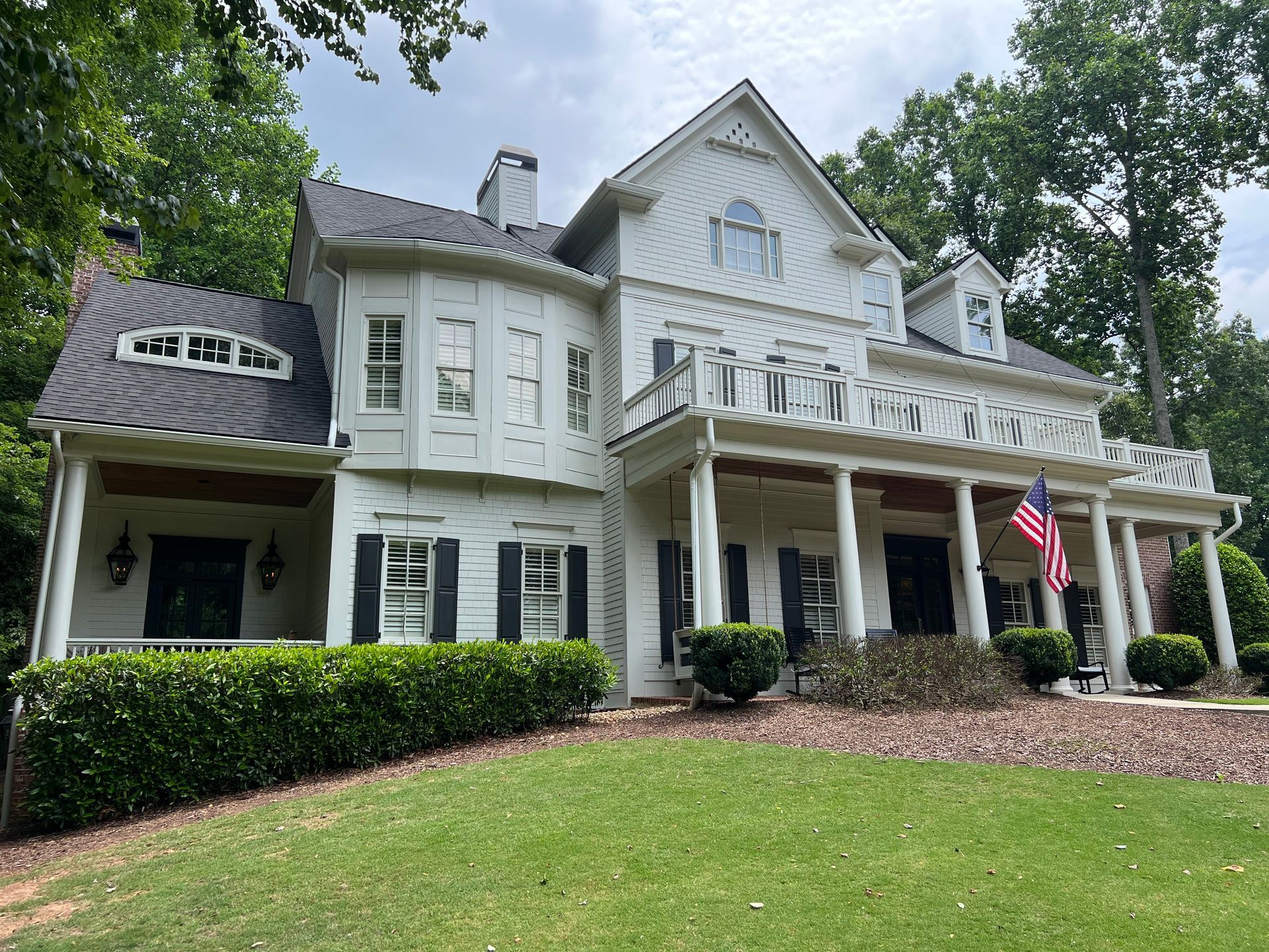 A large white house with a large porch and an american flag in front of it.