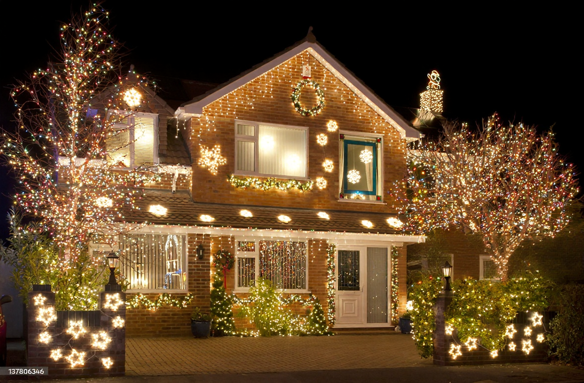 House decorated with Christmas lights at night, with illuminated trees and star-shaped accents.