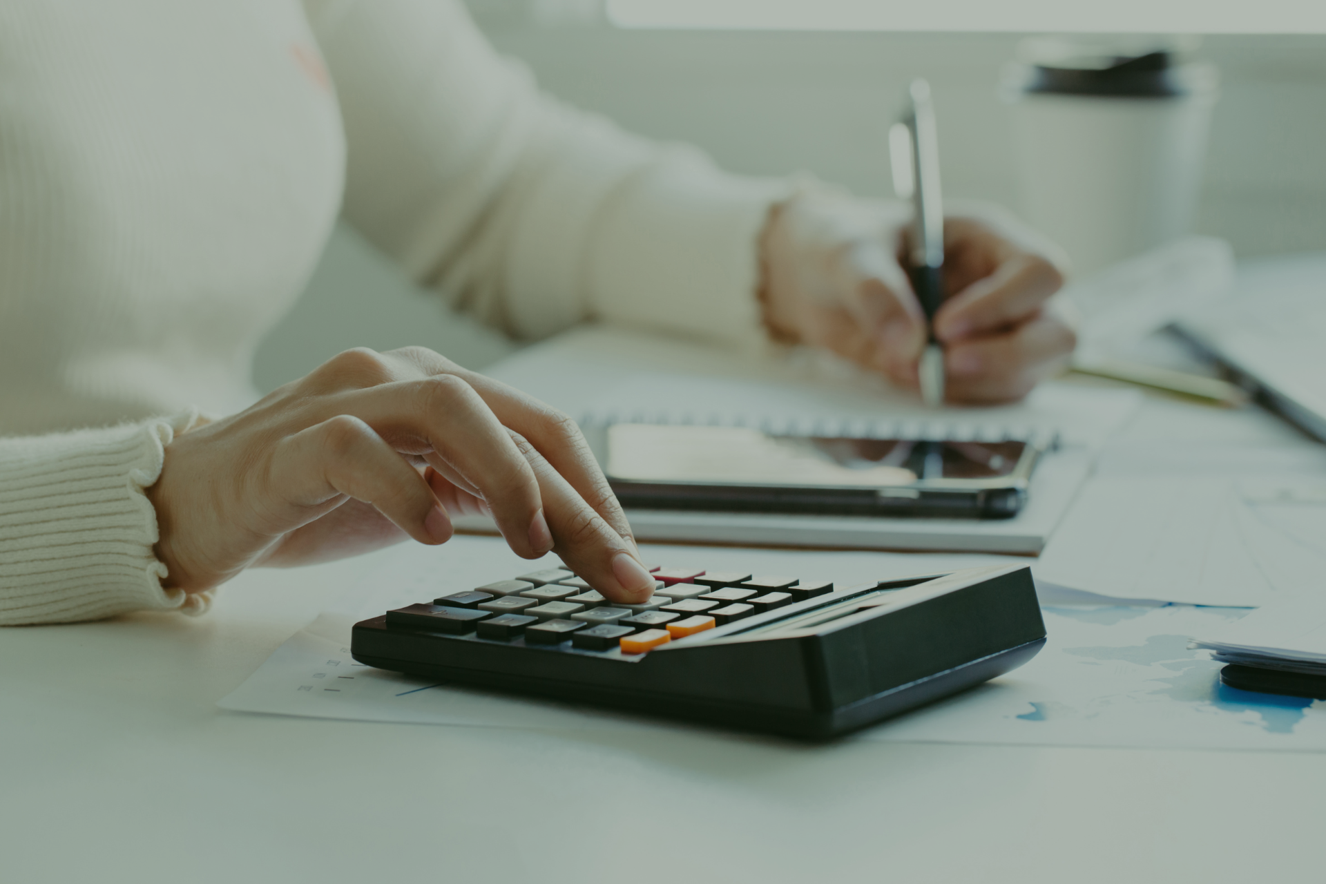 A woman is using a calculator and writing on a piece of paper.