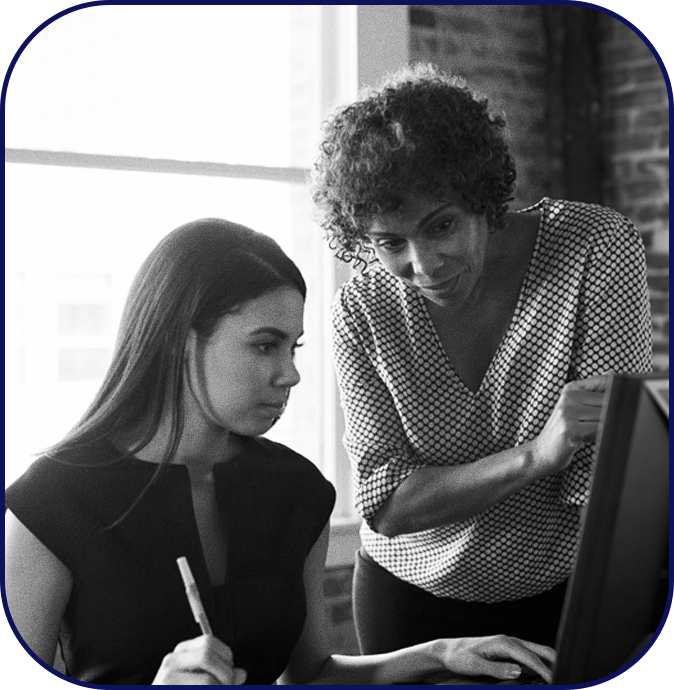 A woman guiding her mentee as they look through her work computer