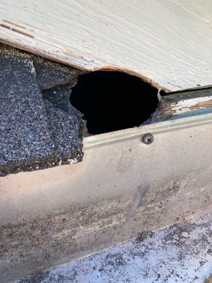 Severely rotted wooden corner trim on a white house exterior, with exposed damaged boards.