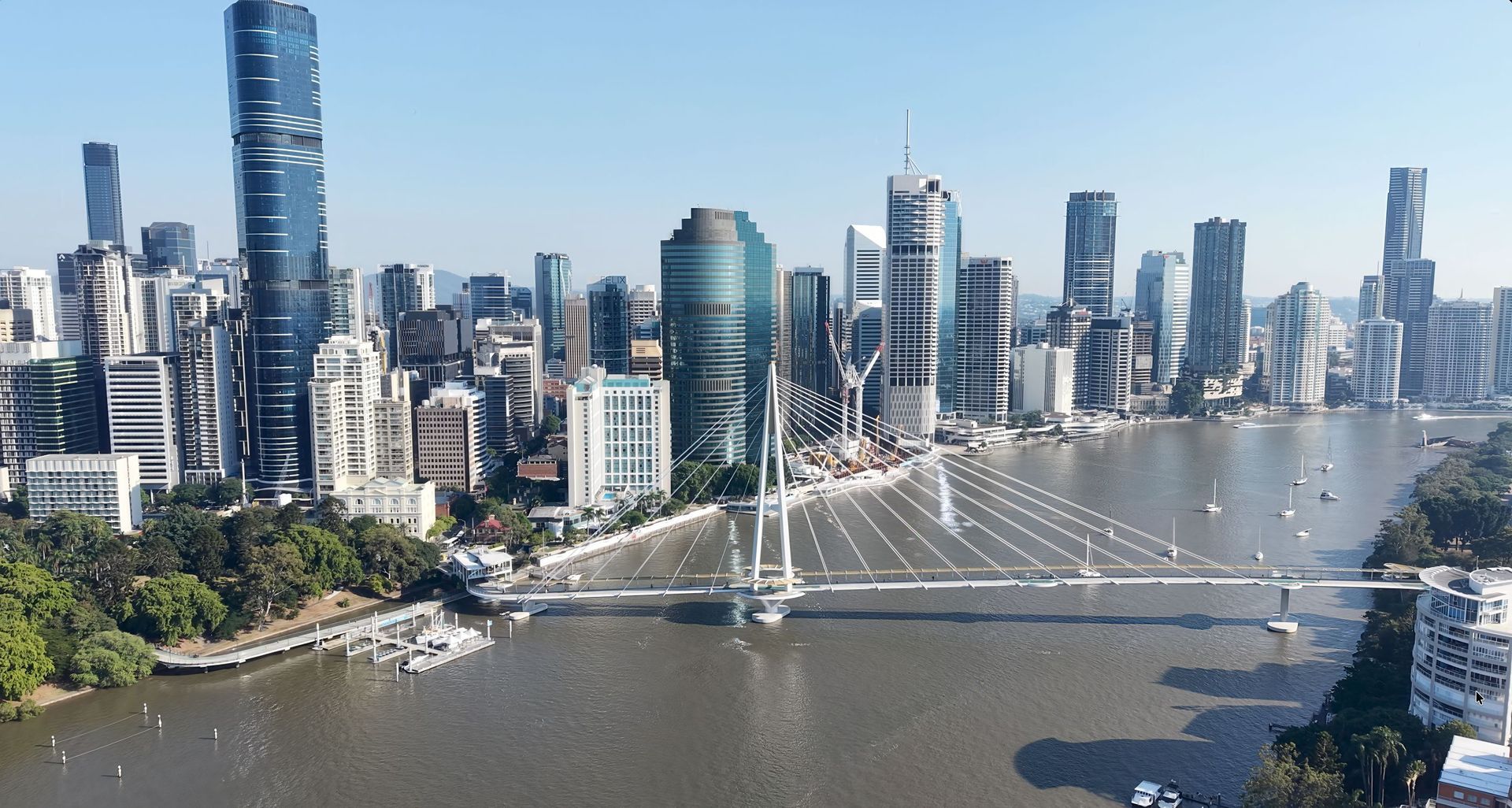 City skyline over a wide river with a cable-stayed bridge under a clear blue sky.