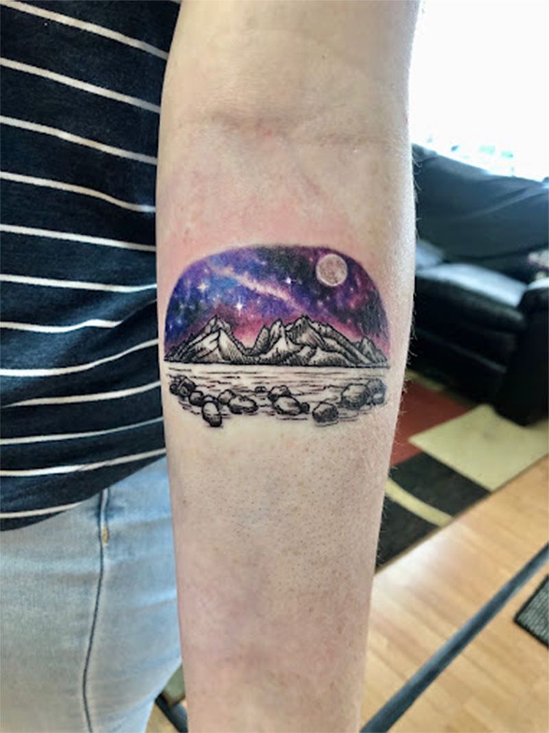 A person has a tattoo of mountains and a moon on their forearm.