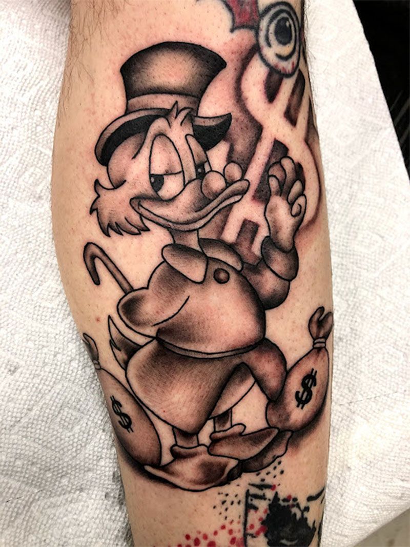 A tattoo of mr. duck holding a bag of money on a leg.