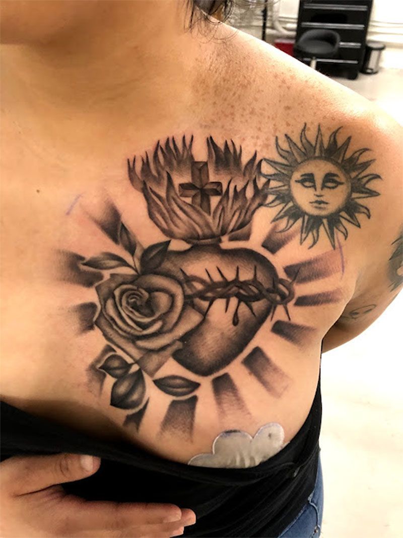 A woman has a tattoo of a heart with thorns and a rose on her chest.