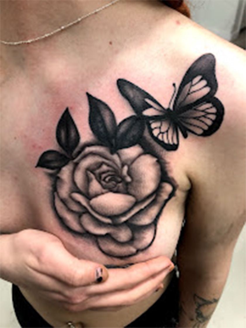 A woman has a tattoo of a rose and a butterfly on her chest.