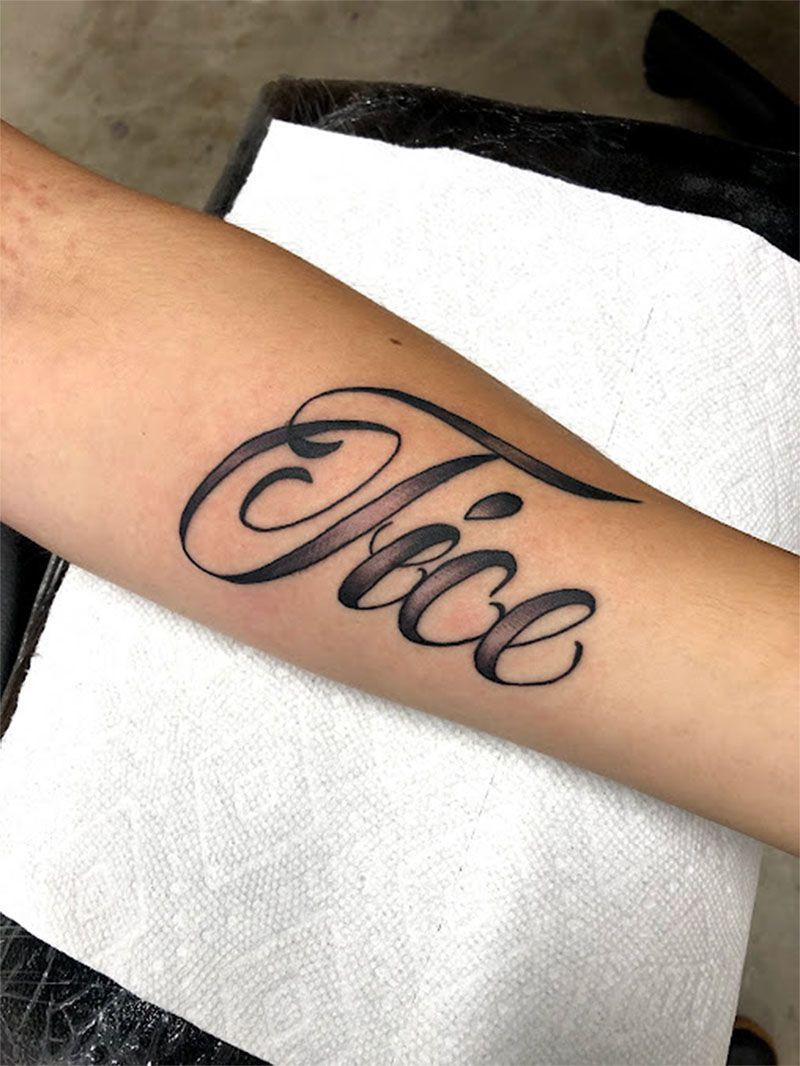 A person has a tattoo of the word trice on their forearm.