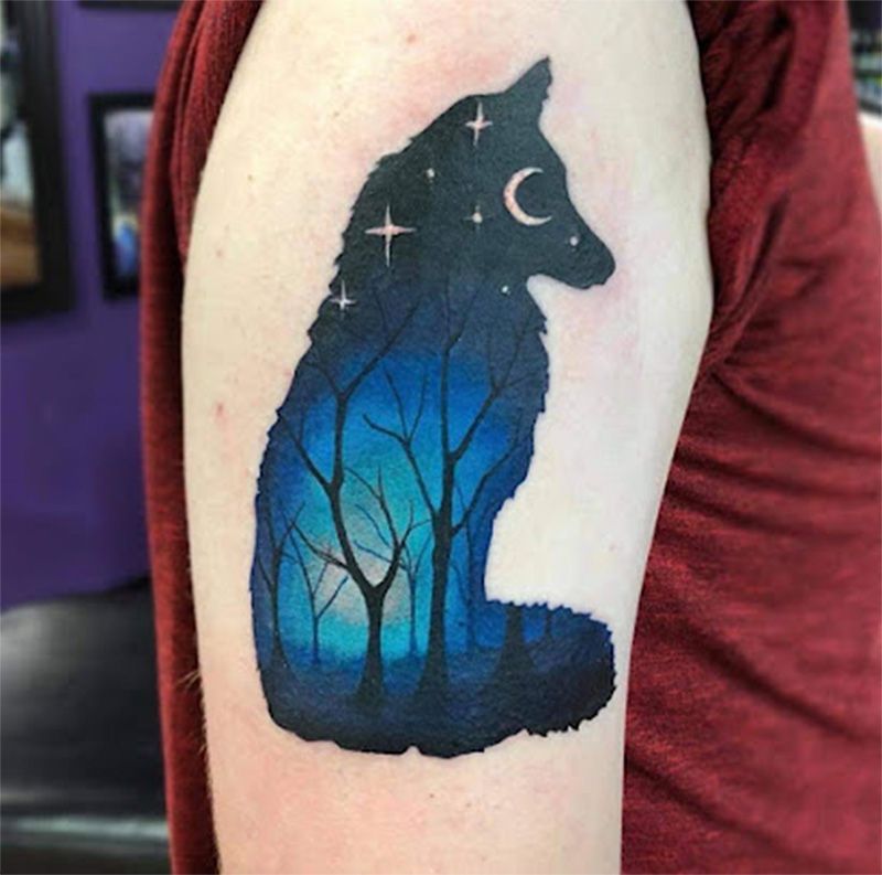 A person has a tattoo of a wolf and trees on their arm.